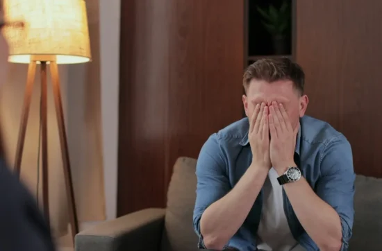 person seated on a sofa with their hands covering their face