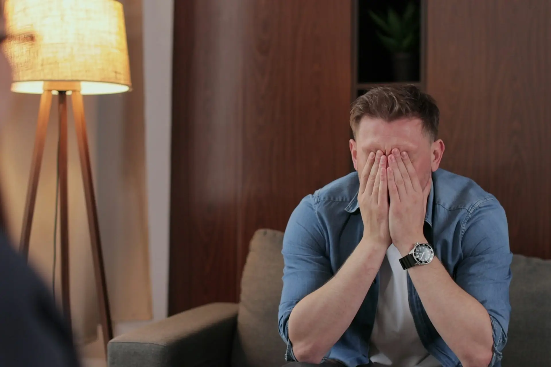 person seated on a sofa with their hands covering their face